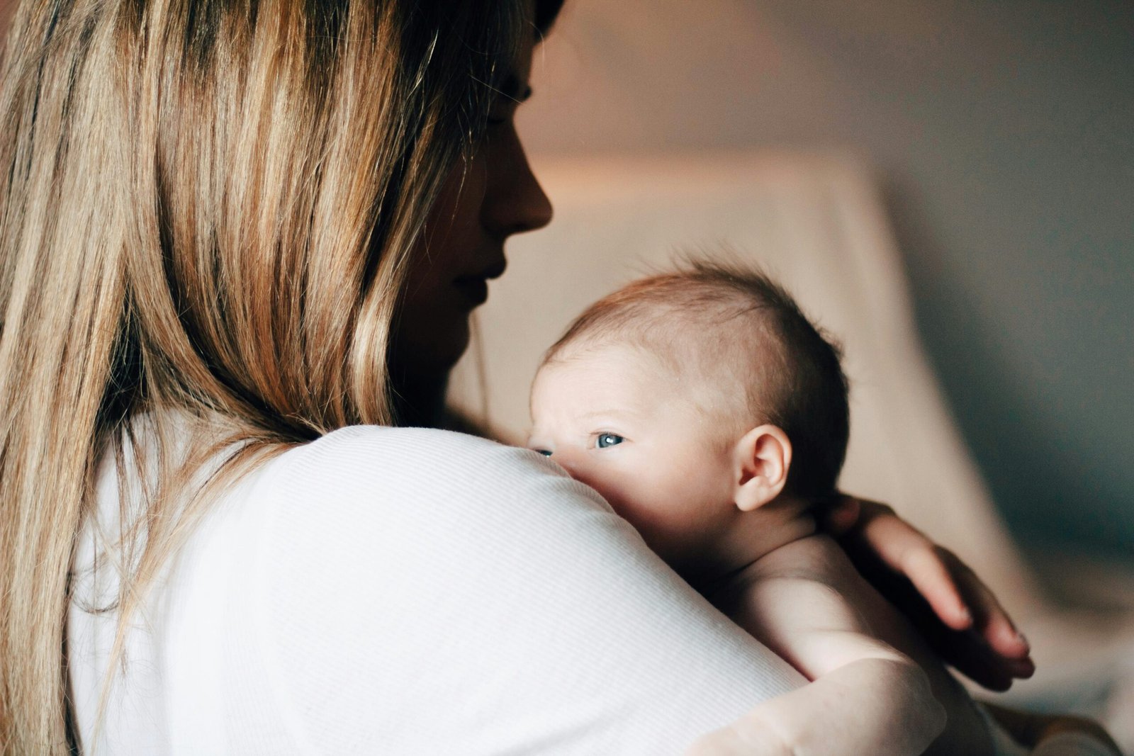 A mother resting in soft morning light while her caregiver quietly settles the newborn nearby